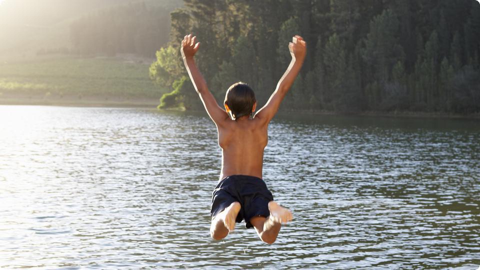 Pojke hoppar från brygga ner i sjö.