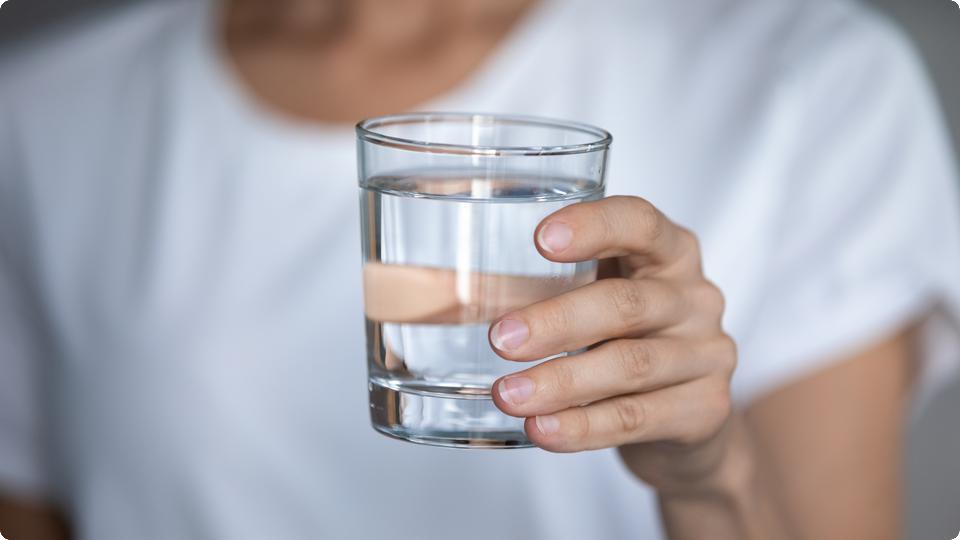 Hand håller i dricksglas med vatten.